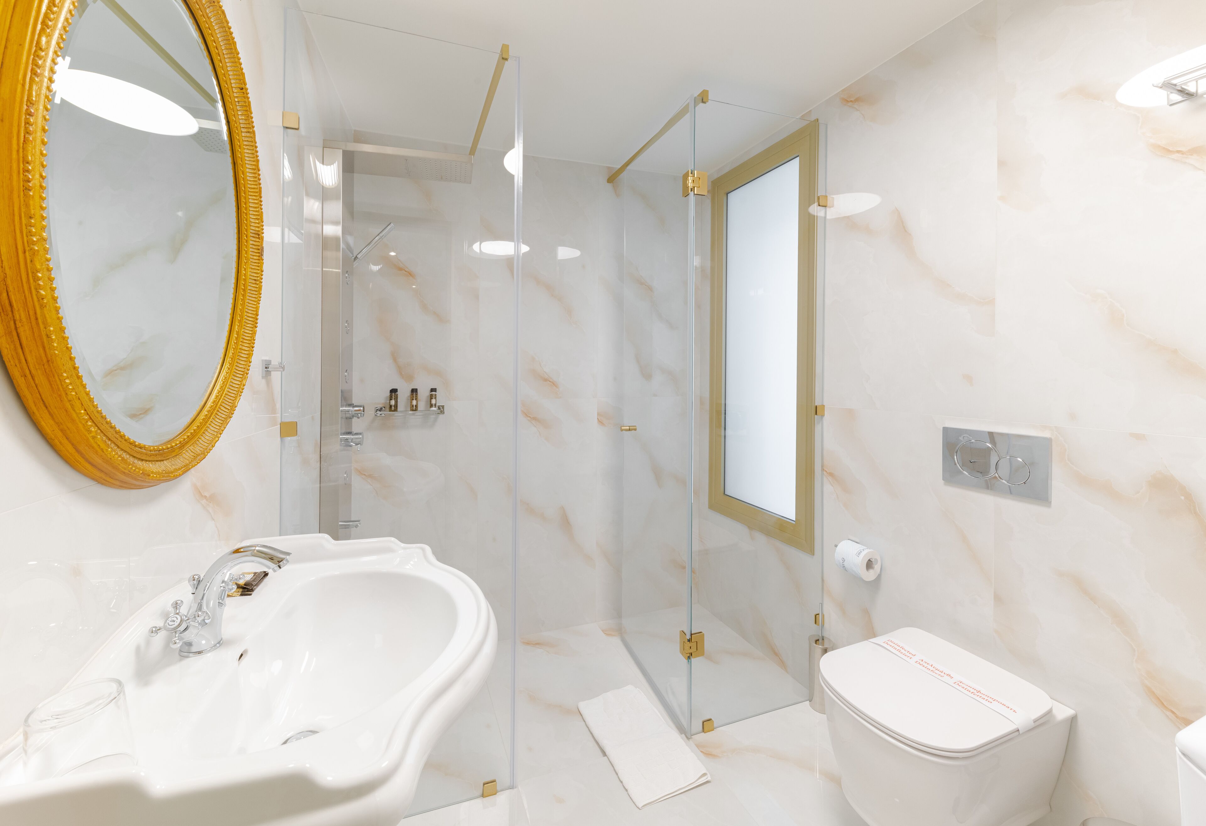 A modern bathroom with a marble sink, a toilet, and a glass-enclosed shower.