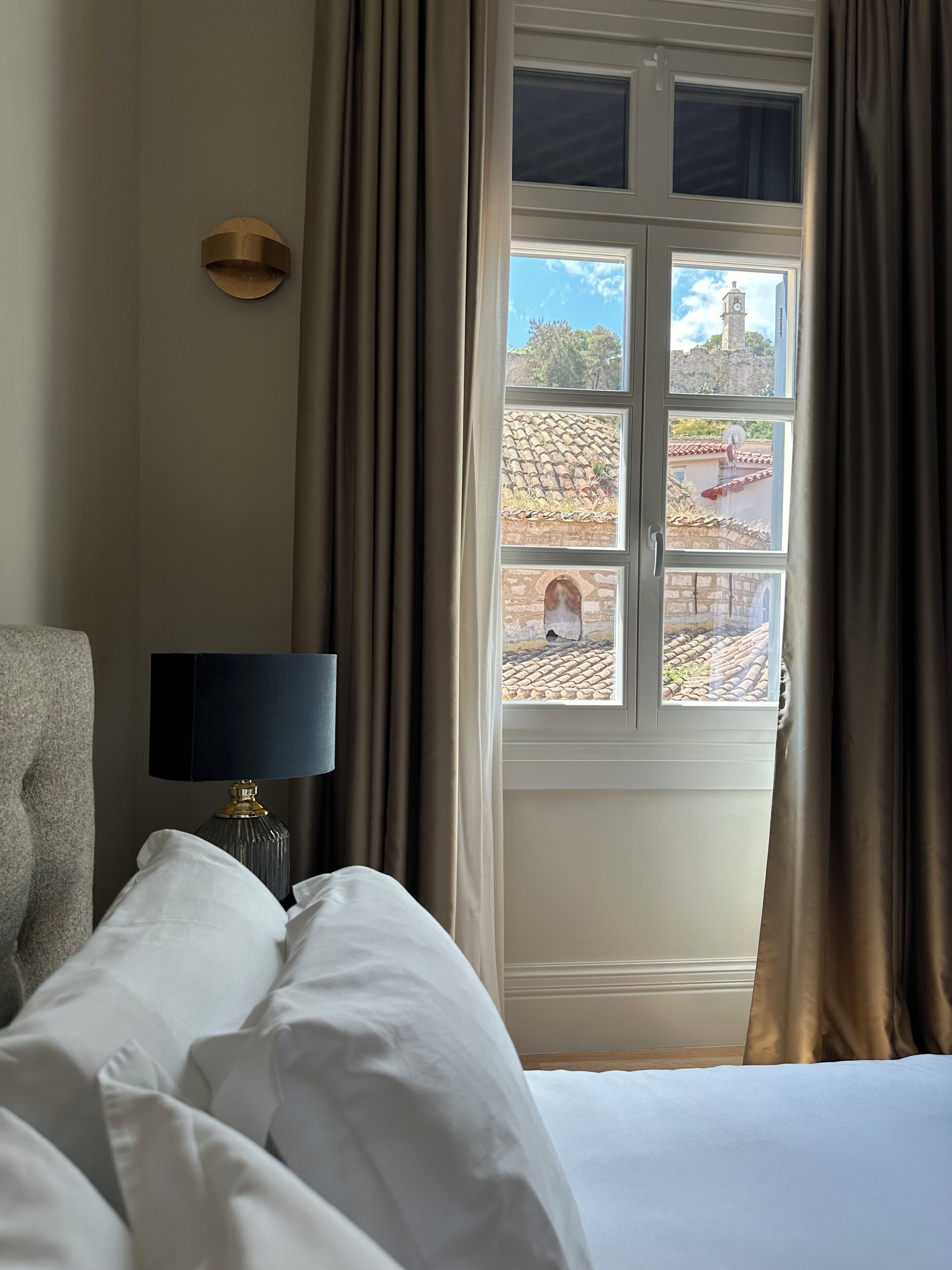 A hotel room with a bed, a lamp, and a window with curtains.