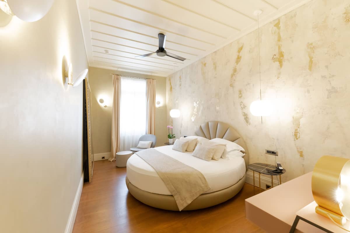 A modern bedroom with a round bed, a ceiling fan, and a bedside table with a lamp.