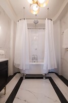Un baño moderno con una bañera independiente, suelo de mármol y cortina de ducha.
