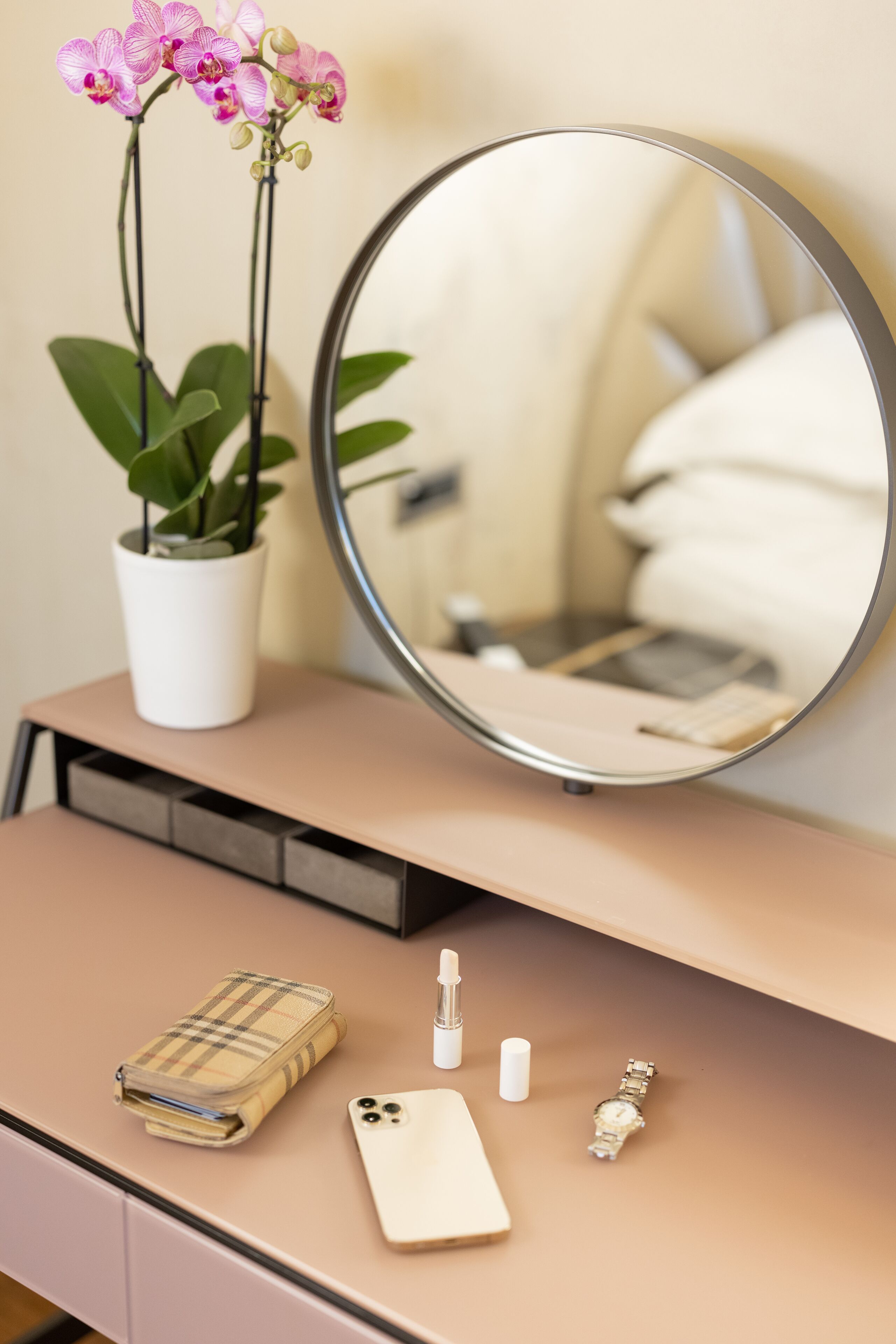 Un coin beauté avec un miroir, une orchidée en pot, une montre, un téléphone et une trousse de maquillage.