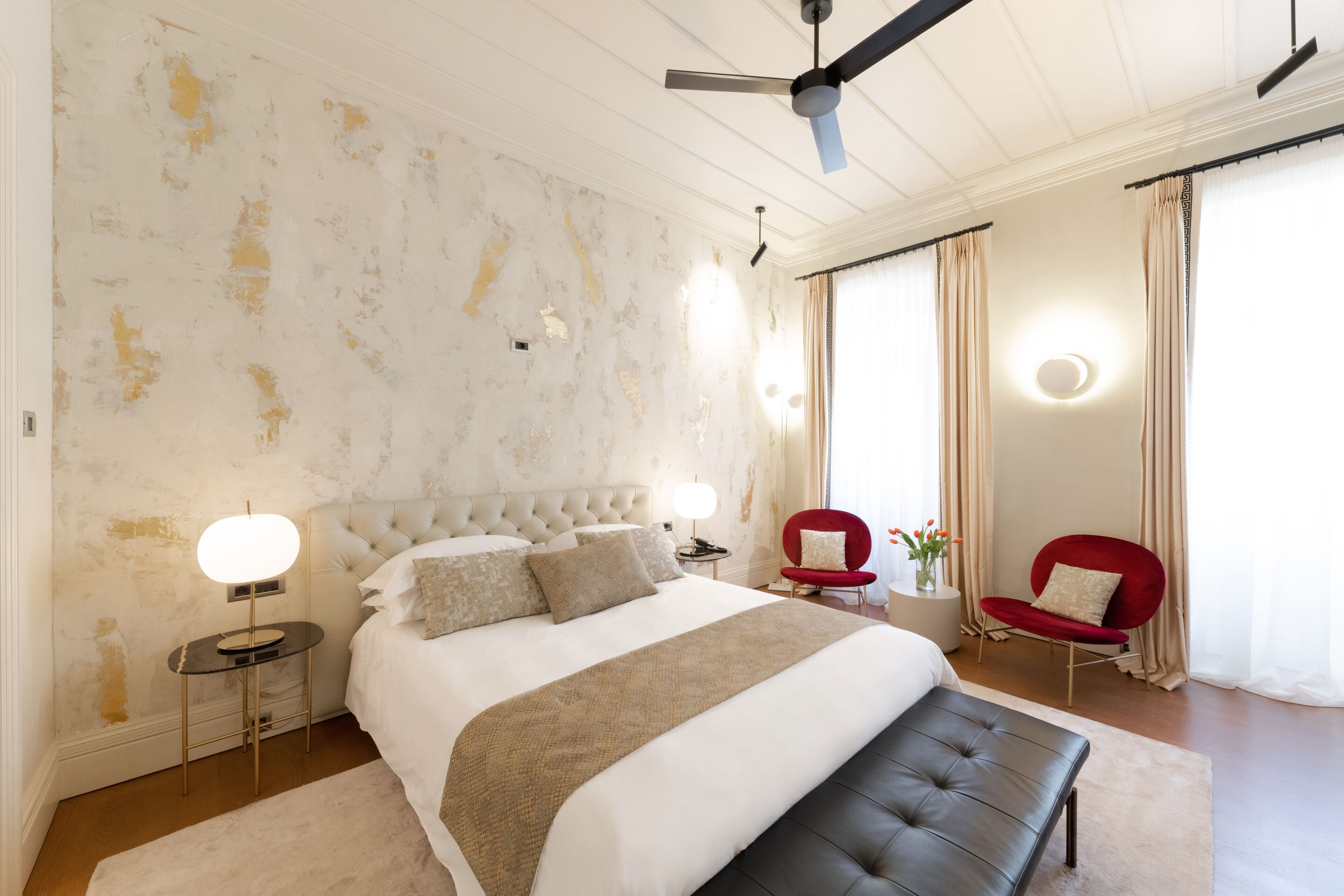 Un dormitorio con una cama grande, una silla roja, una mesa redonda y un ventilador de techo.