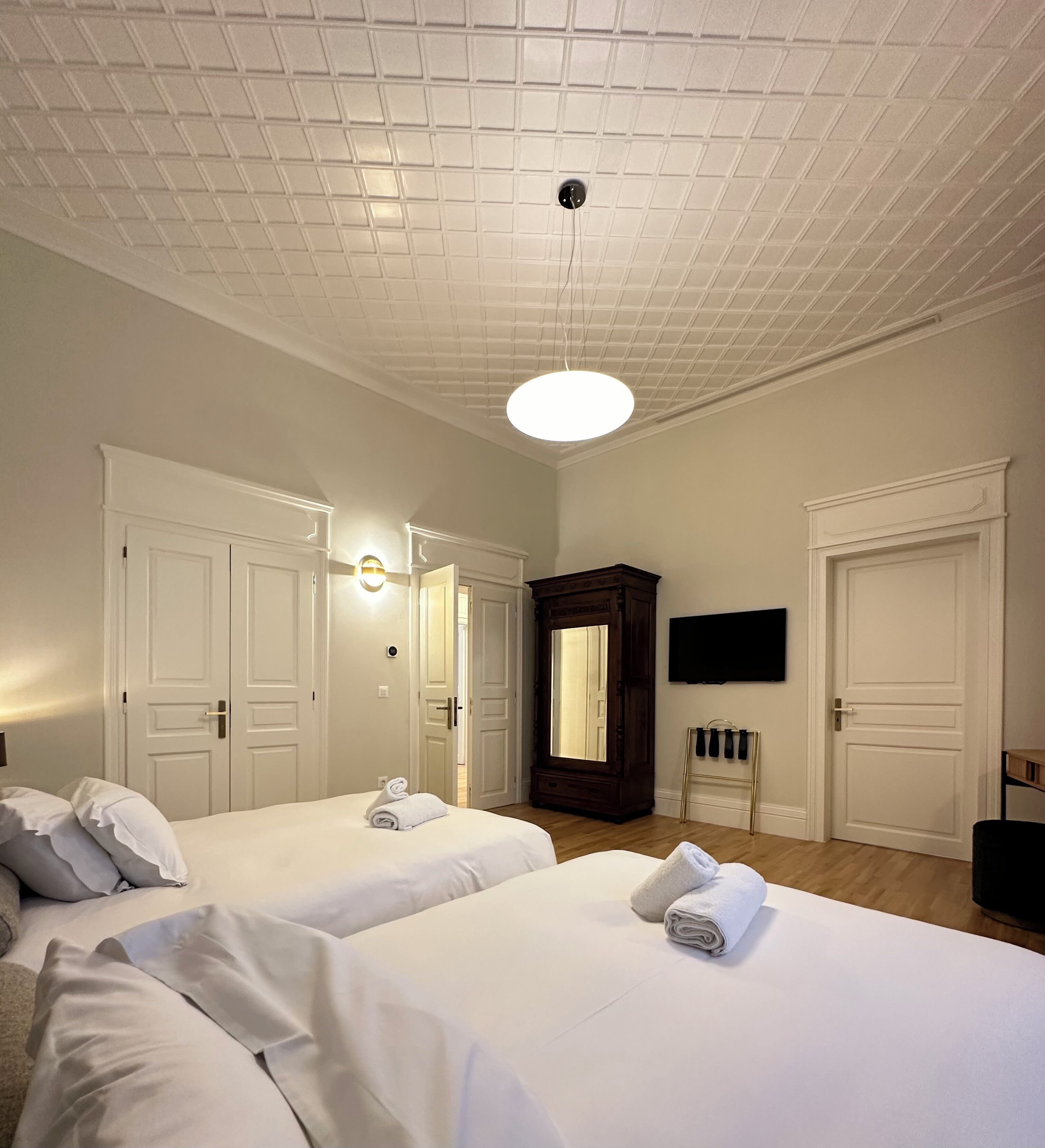 A hotel room with two beds, a large mirror, a flat-screen TV, and a wooden cabinet.