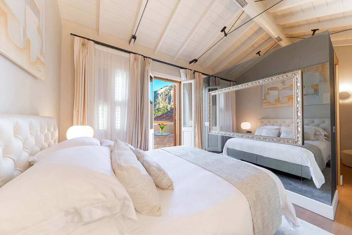 A bedroom with a large bed, a mirrored wardrobe, and a view of a mountainous landscape through the window.