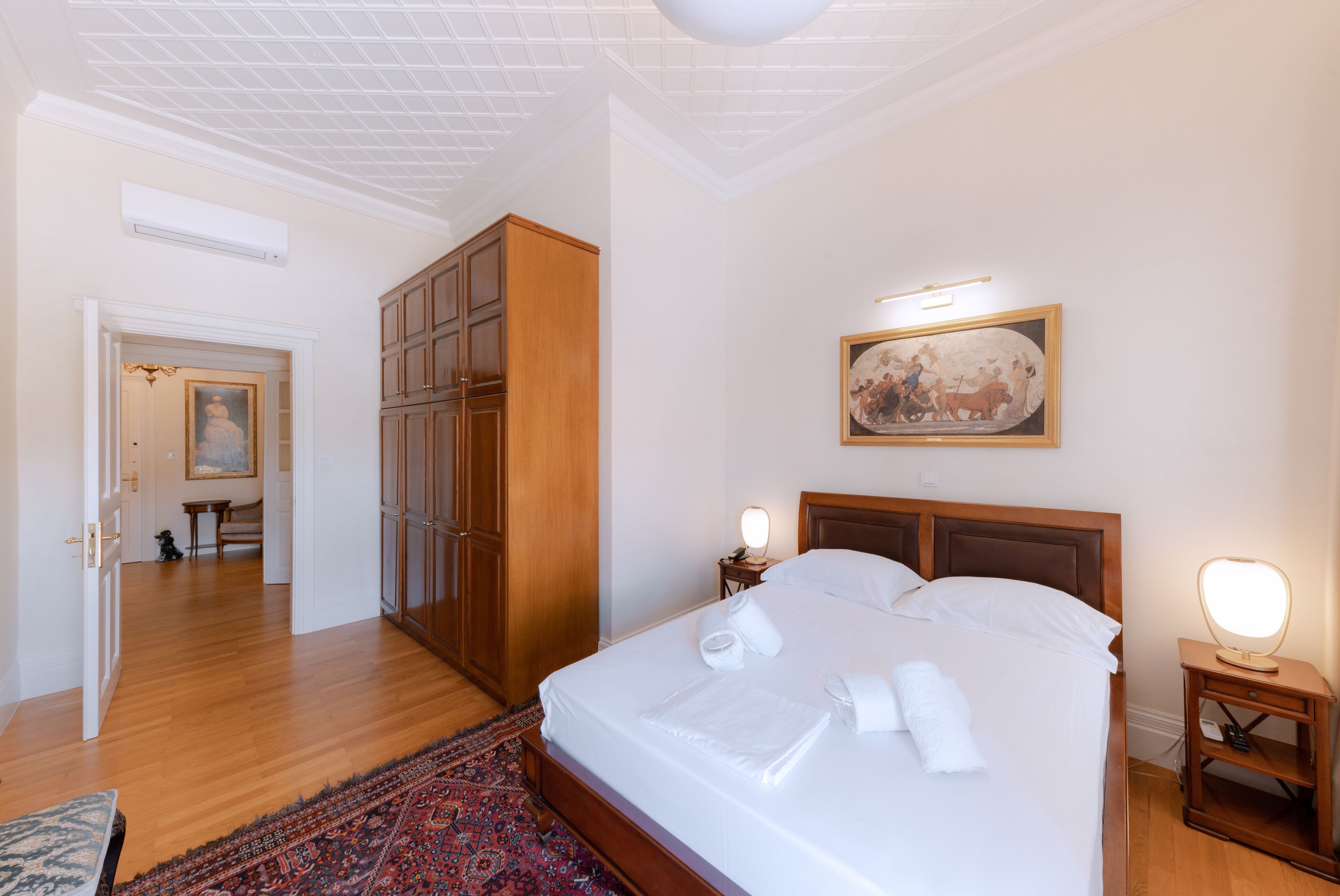 Une chambre d’hôtel avec un grand lit, une armoire en bois, un tableau au mur et une table de chevet avec une lampe.