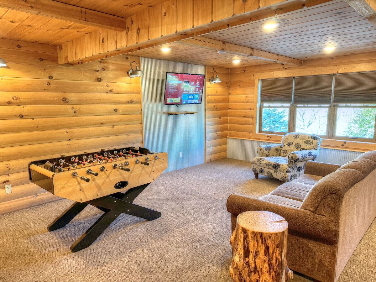 Una habitación acogedora con detalles de madera, una mesa de fútbol, un sofá y un televisor montado en la pared.