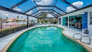 En pool med tak, solstolar, utsikt över vattnet och en byggnad med blå fasad.