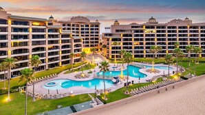 Un hotel de varios pisos, una piscina central y palmeras.