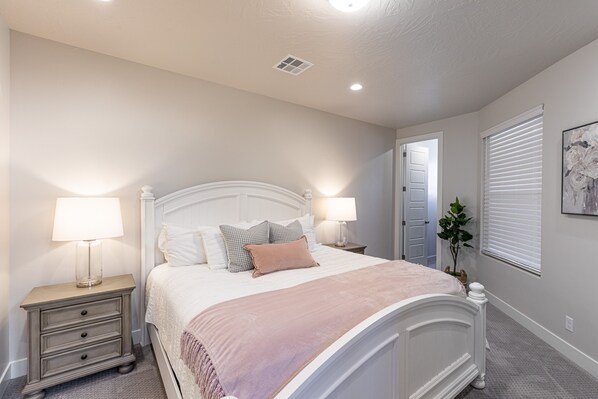 Un dormitorio con cama, mesitas de noche y una puerta que da a otra habitación.