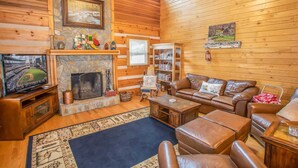 A cozy log cabin interior with a stone fireplace, leather furniture, and a television. - Rustic Cabin in Heart of Boone (Boone)