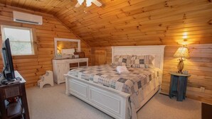 A cozy bedroom with a wooden ceiling, a bed with a quilt, a bedside lamp, and a TV on a dresser. - Rustic Cabin in Heart of Boone (Boone)