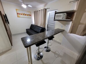 A compact living space with a kitchenette, a black sofa, a painting on the wall, and a ceiling fan.