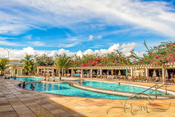 A pool area with multiple pools, lounge chairs, and a covered seating area with umbrellas.