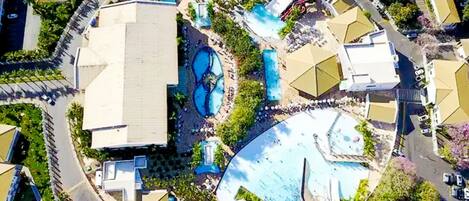 An aerial view of a resort with multiple swimming pools, a water slide, and a large building.