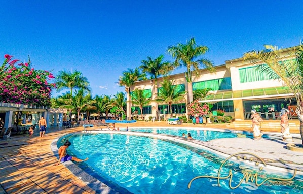 A swimming pool with lounge chairs, palm trees, and a building with large windows.