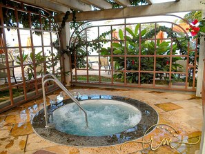 A hot tub with a metal railing, surrounded by a tiled floor and a metal fence with plants. - Lacqua diRoma RM Hospedagem (Caldas Novas)