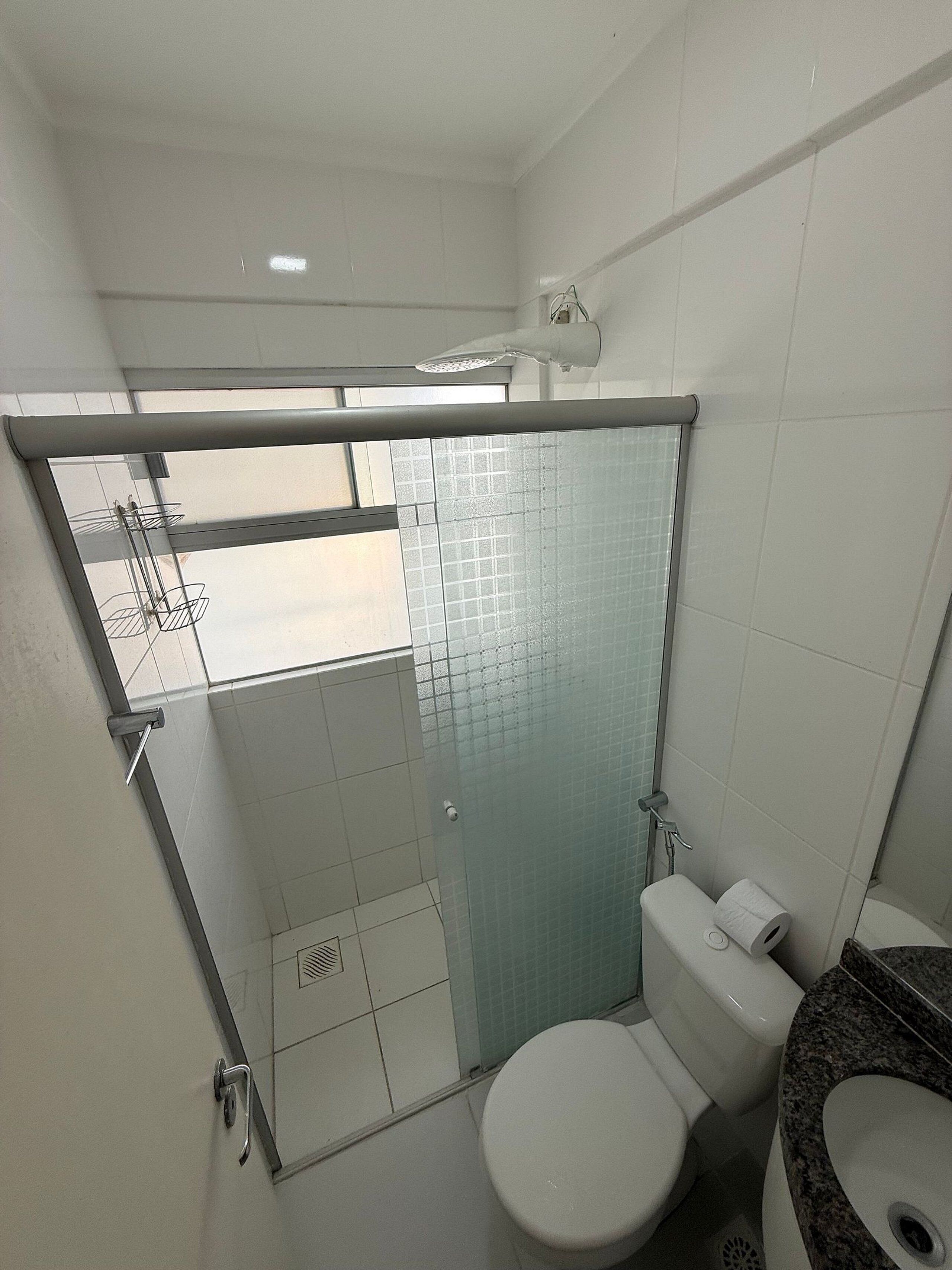 A bathroom with a glass shower enclosure, a toilet, and a sink.