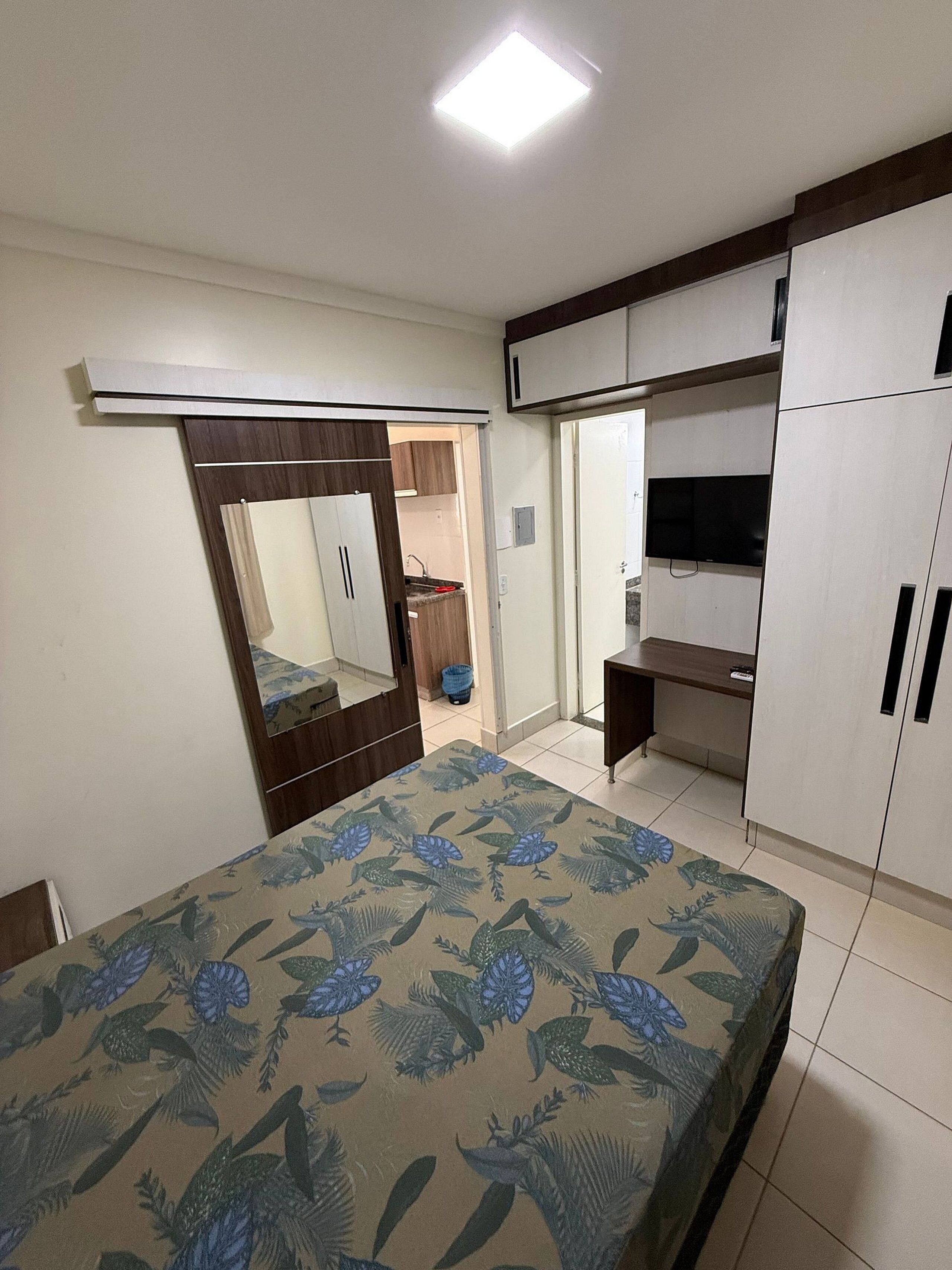 A bedroom with a bed, wardrobe, mirror, and a television.