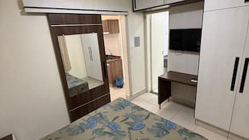 A bedroom with a bed, wardrobe, mirror, and a television.