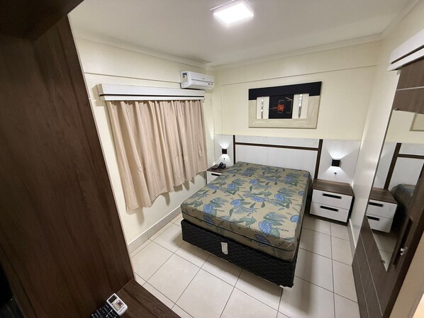 A bedroom with a bed, bedside tables, an air conditioning unit, a mirror, and a curtain.