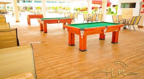 A pool table area with chairs and tables, wooden flooring, and a view of the outdoor area.