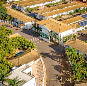 A resort with multiple buildings, a central road, and a pool area surrounded by palm trees.