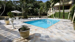 A swimming pool with lounge chairs and tables, surrounded by potted plants and palm trees. - Chácara Bosque dos Pássaros - Santa Isabel (Santa Isabel)