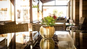 Une table en verre sur laquelle se trouve un vase doré contenant des plantes vertes et une fleur rouge.
