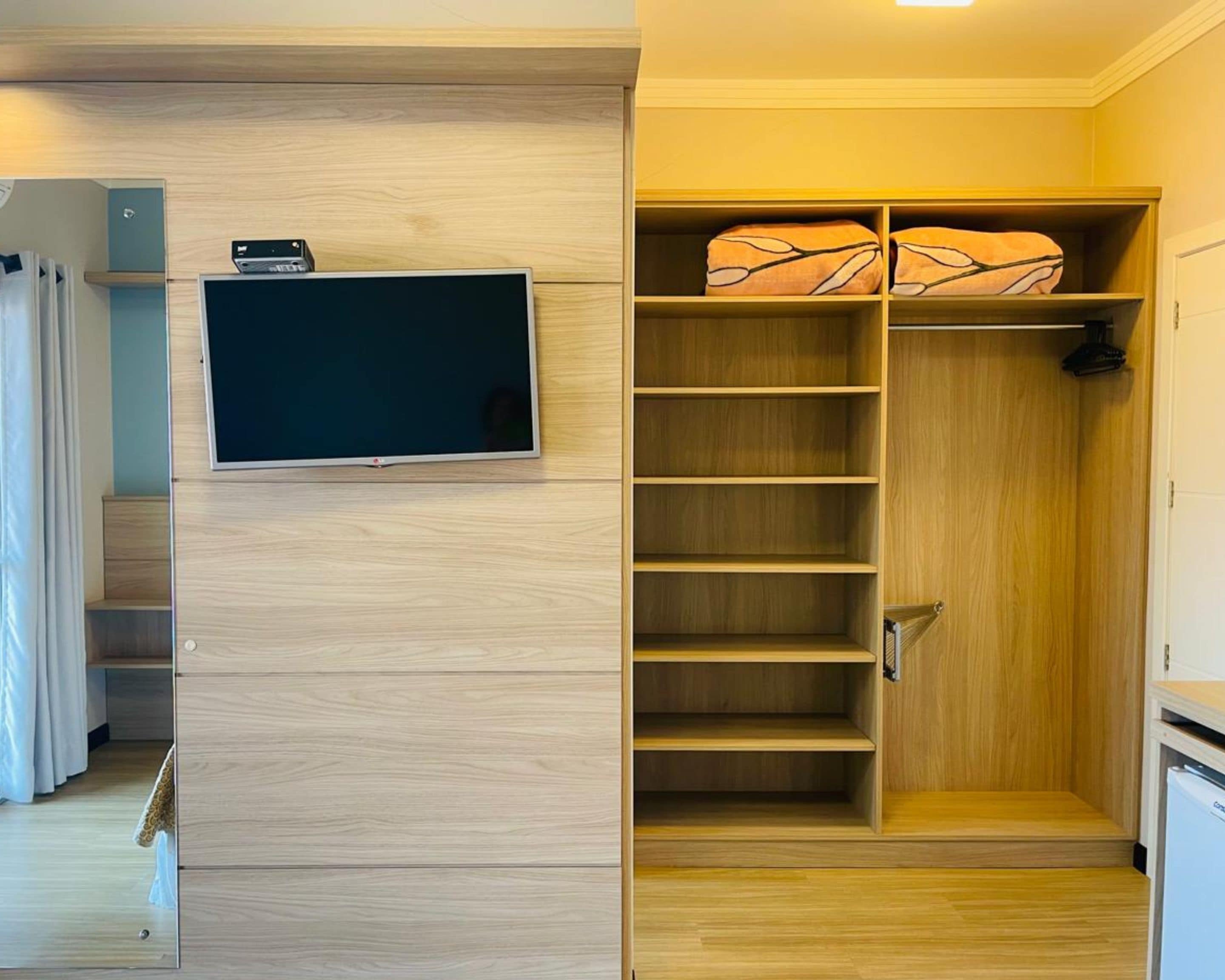 A modern room with a built-in TV, wooden shelving, and a wardrobe with hanging space.