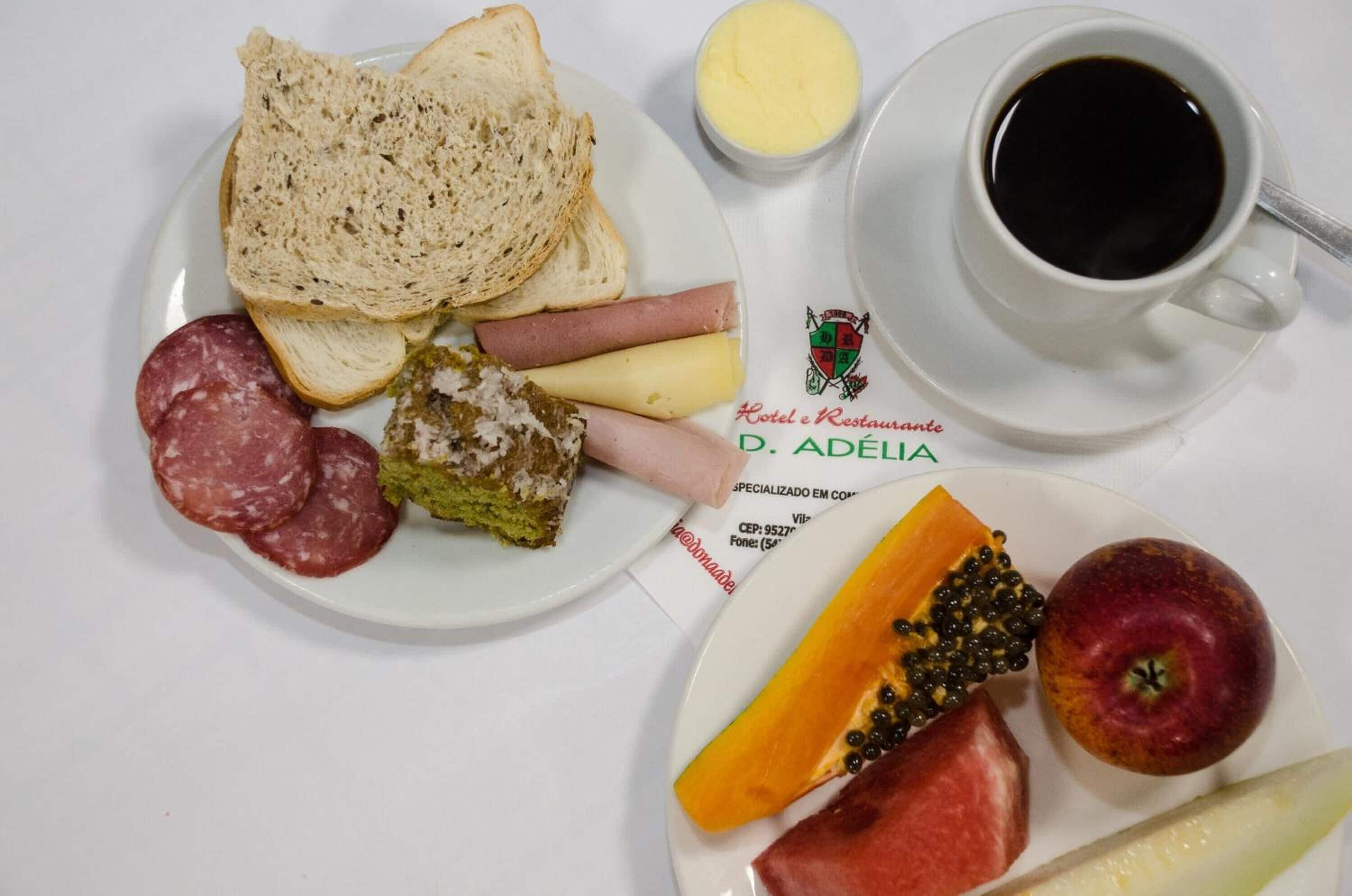 Une assiette de petit-déjeuner avec du pain, de la charcuterie, du fromage et des fruits, et une tasse de café sur une table.