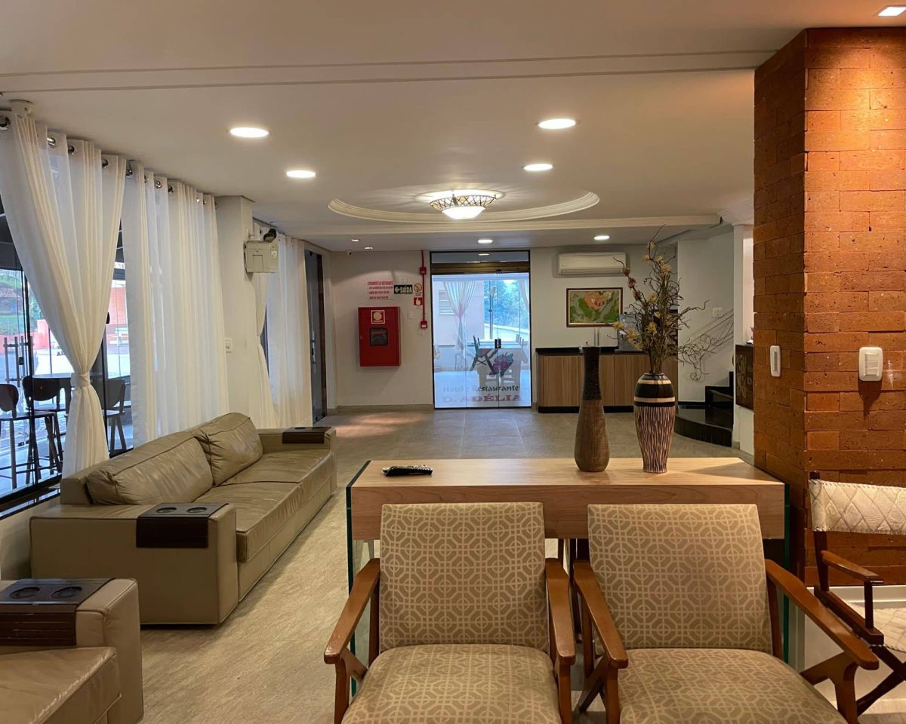 Recepció d'hotel amb taulell d'admissió, zona d'estar amb sofàs i butaques, un vas amb flors i un extintor a la paret.