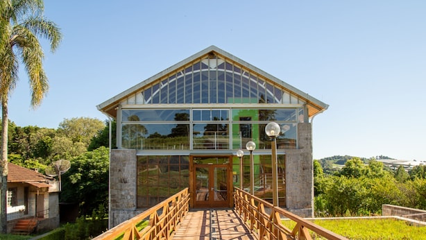 Un bâtiment moderne doté d’une façade en verre, d’une passerelle en bois menant à l’entrée et offrant une vue sur la verdure environnante.