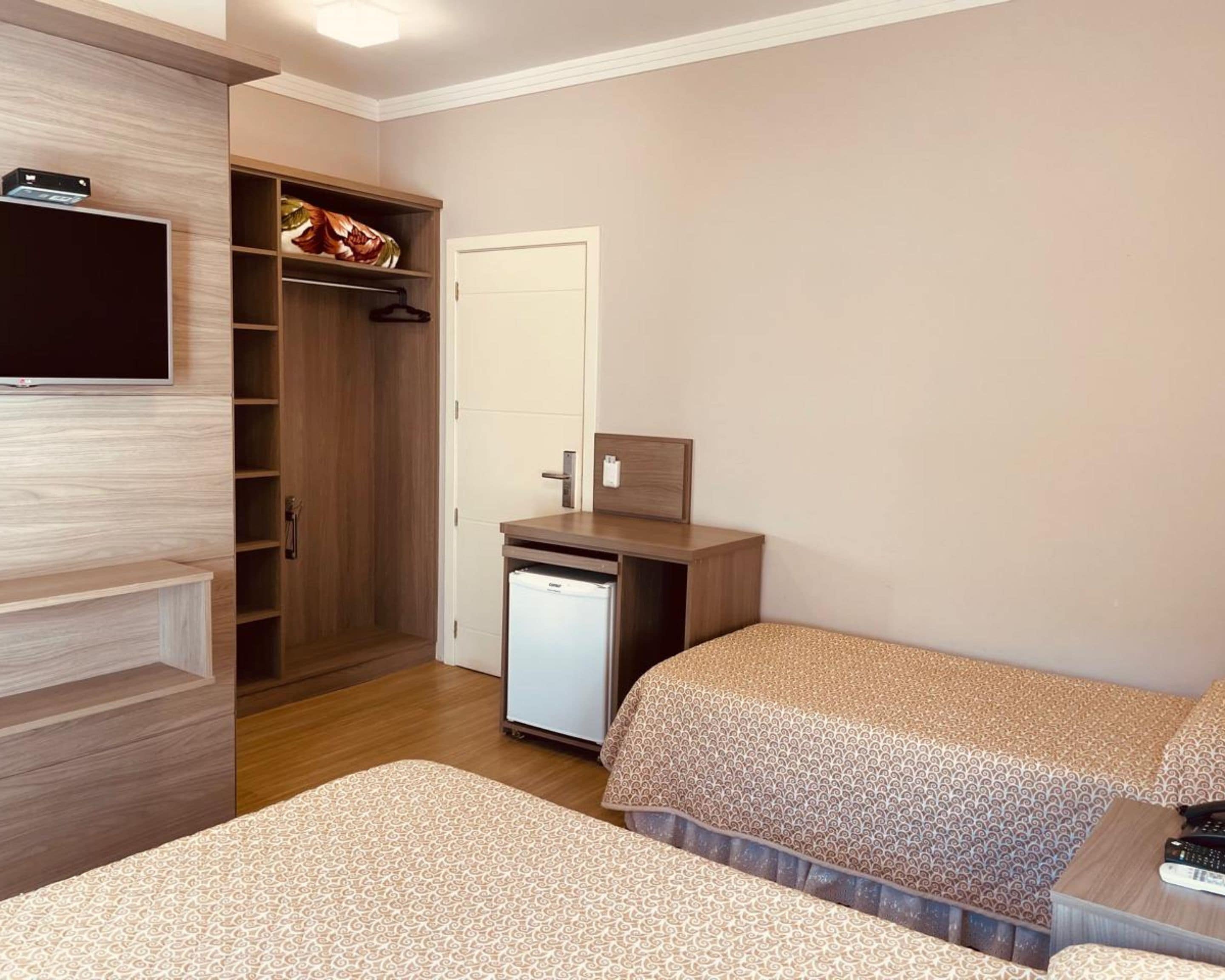 Une chambre avec deux lits, une armoire, un petit réfrigérateur et un téléviseur fixé au mur.