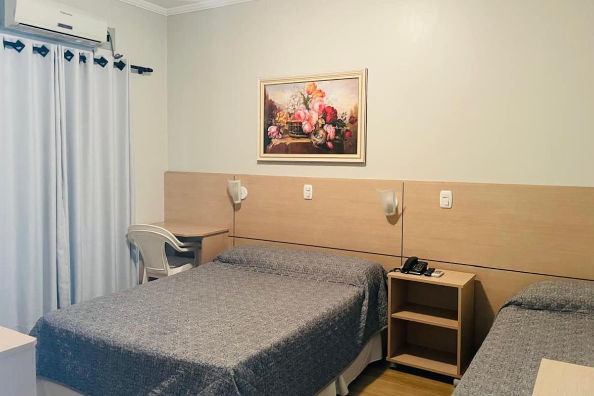 Habitación de hotel con dos camas, un escritorio, una silla, un cuadro en la pared y un teléfono en la mesita de noche.