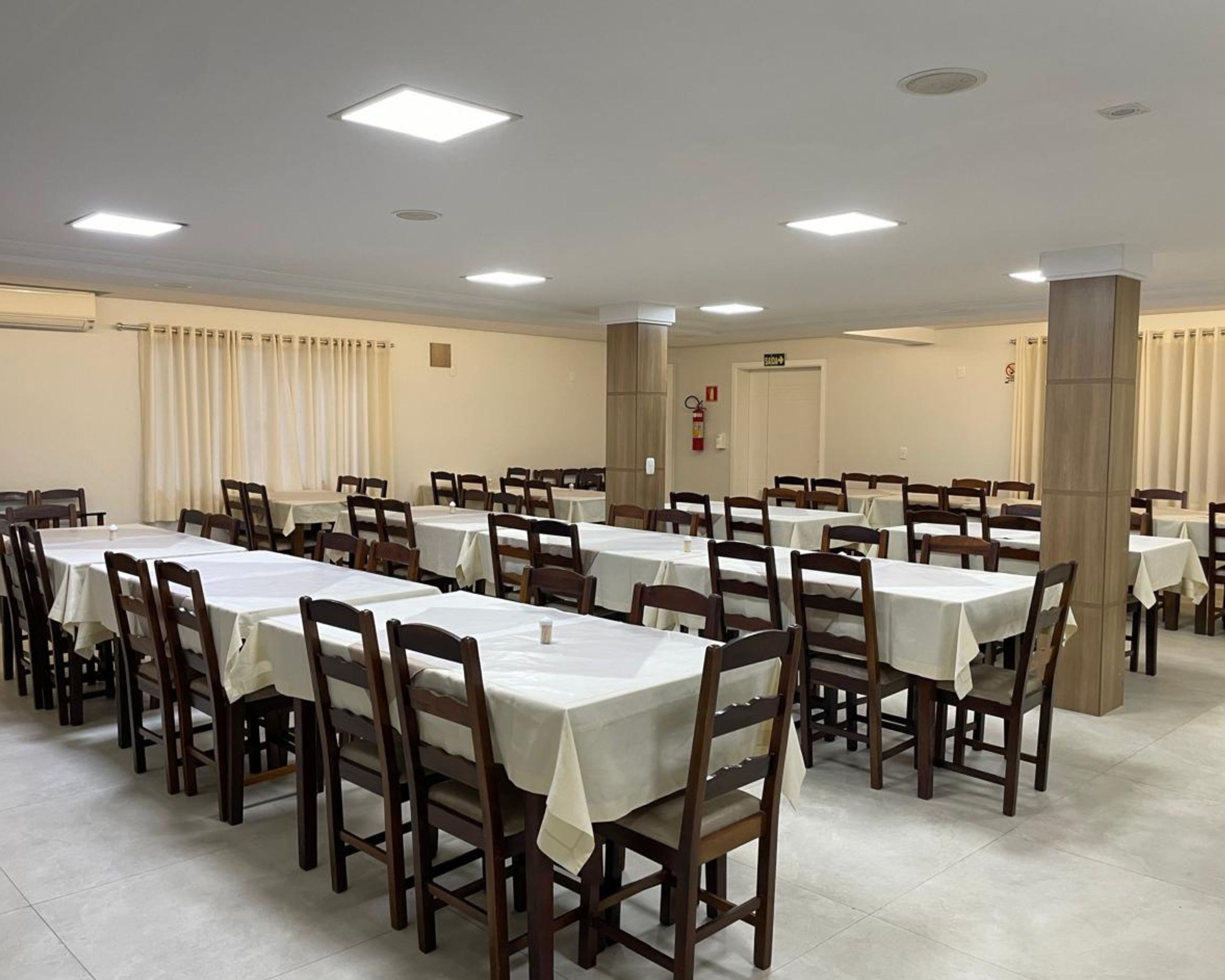 A large, well-lit conference room with multiple tables and chairs, arranged in rows.