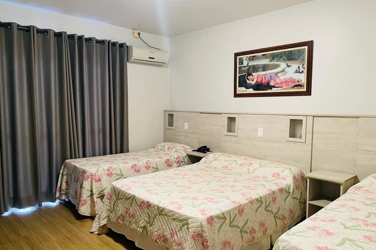 Habitación de hotel con dos camas individuales, una mesita de noche pequeña, aire acondicionado instalado en la pared y un cuadro enmarcado.