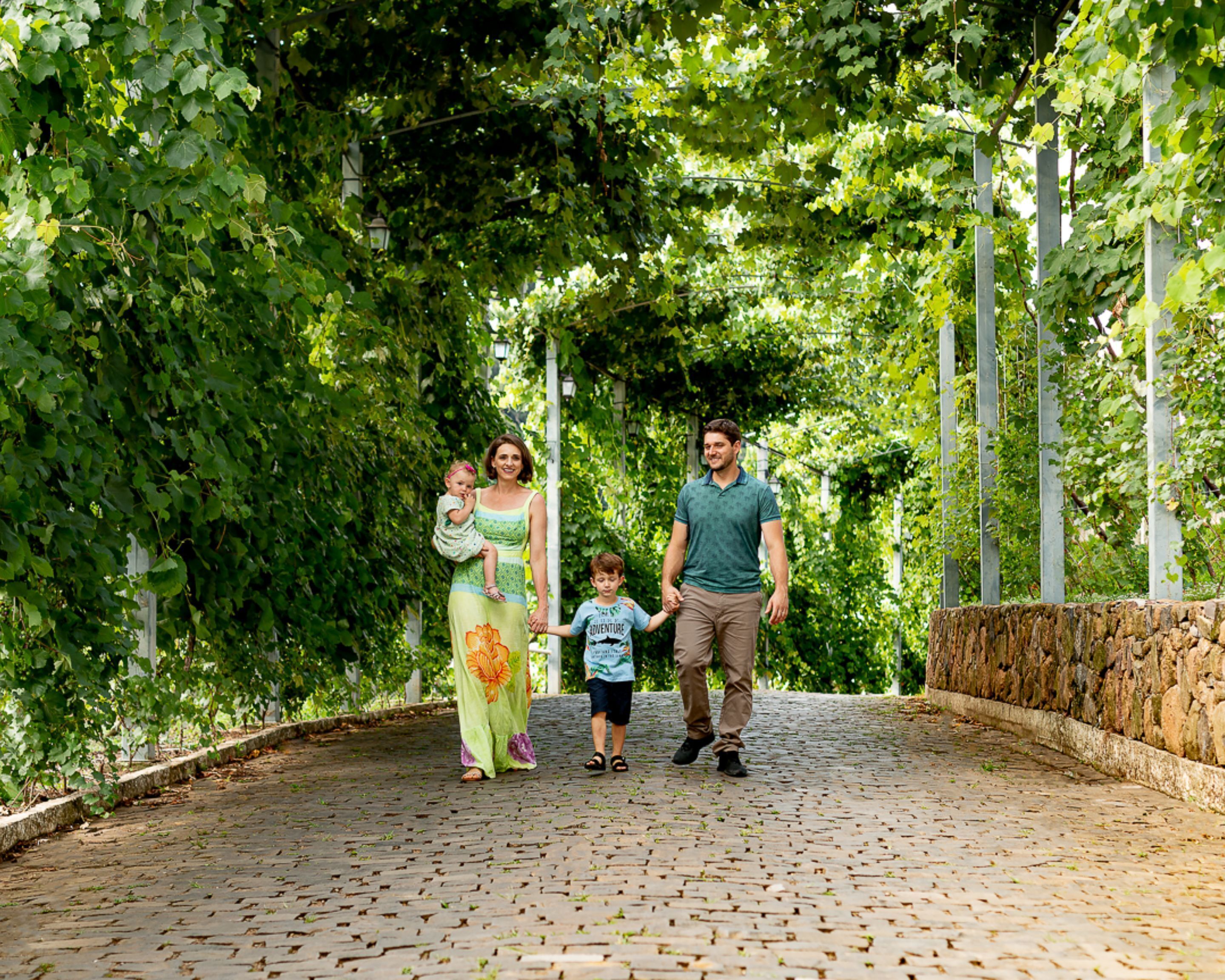 A family walking on a cobblestone path surrounded by lush greenery and a stone wall.