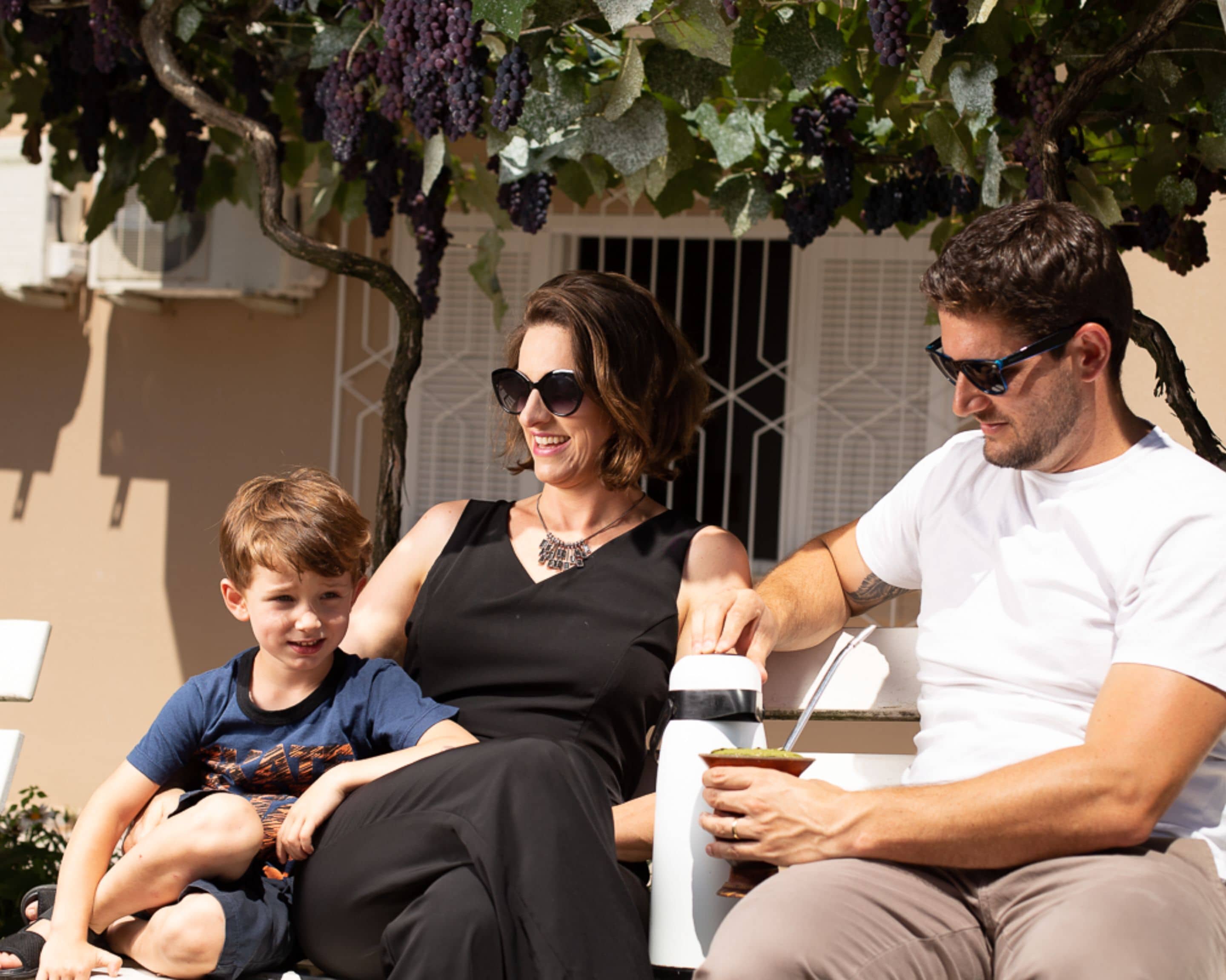 A family of three seated outdoors with a table in front of them.