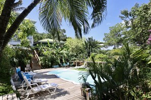 Relax by the serene pool surrounded by lush greenery and palm trees, with lounge chairs and a wooden deck.