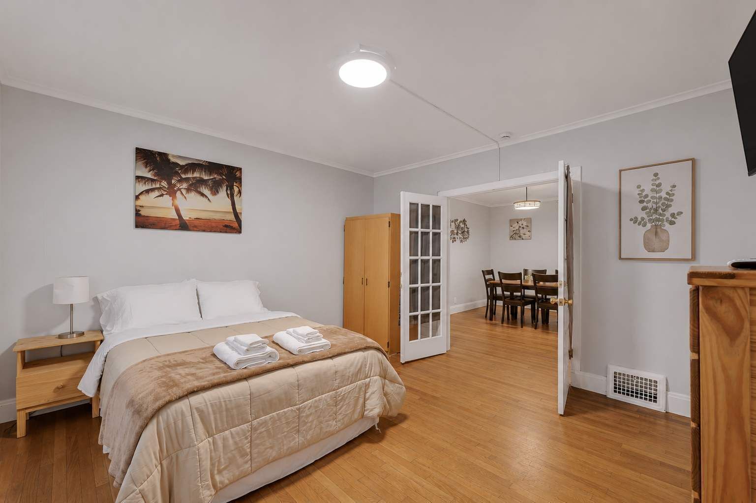 Een slaapkamer met een bed, nachtkastje en een schilderij van een strand.
