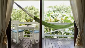 En træterrasse med et hvidt bord og stole, en hængekøje og frodig vegetation i baggrunden.