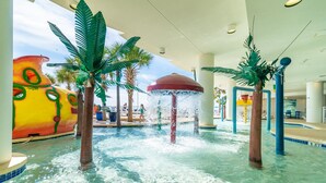 Un parc aquatique intérieur avec des palmiers, un toboggan coloré et une fontaine.