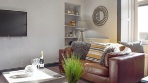 Ein Wohnzimmer mit einer Ledersofa, einem Couchtisch mit Pflanze, einem an der Wand befestigten Fernseher und einem Fenster mit Blick.