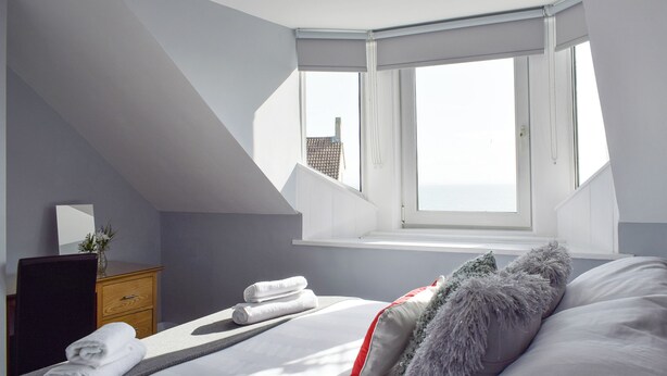 Ein Schlafzimmer mit Bett, Fenster, Kommode und Spiegel.