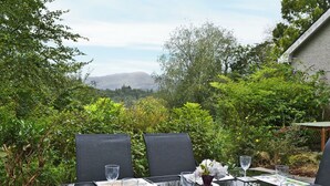 Un espace de restauration en plein air avec une table dressée pour quatre personnes, entouré d’une végétation luxuriante et offrant une vue sur les montagnes.