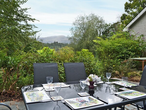 An outdoor dining area with a table set for four, surrounded by lush greenery and a mountain view.