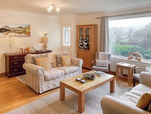 A living room with a sofa, armchairs, a coffee table, a cabinet, and a window with a view.