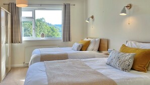 Une chambre d’hôtel avec deux lits, une fenêtre donnant sur un paysage verdoyant et un luminaire fixé au mur.