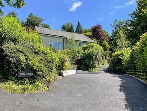 A house named 'Sheilings' surrounded by lush greenery and a paved driveway.