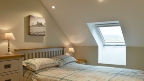 Un dormitorio con cama, dos mesitas de noche, una mesita auxiliar, una ventana con vistas y un cuadro colgado en la pared.